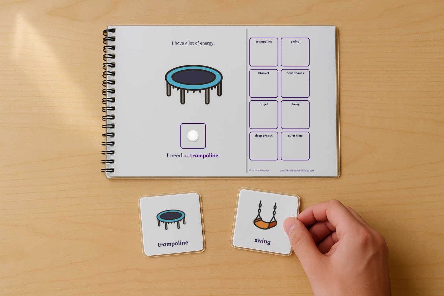 A page of the Sensory Breaks adapted book, laminated and spiral bound, with a child's hand holding a picture card beside it