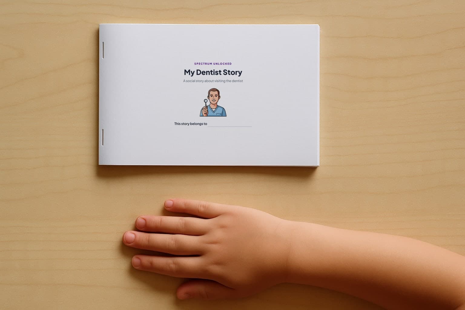 The Going to the Dentist social story printed and stapled into a small booklet, closed on a table with a child's hand beside it