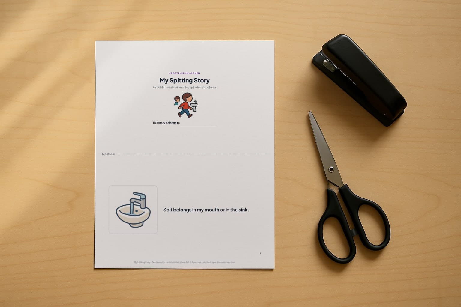 The Spitting social story printed two pages to a Letter sheet, scissors and a stapler beside it before the cut