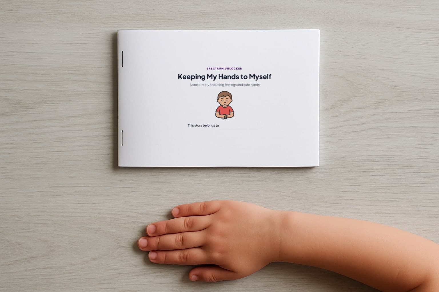 The When I Feel Like Hitting social story printed and stapled into a small booklet, closed on a table with a child's hand beside it