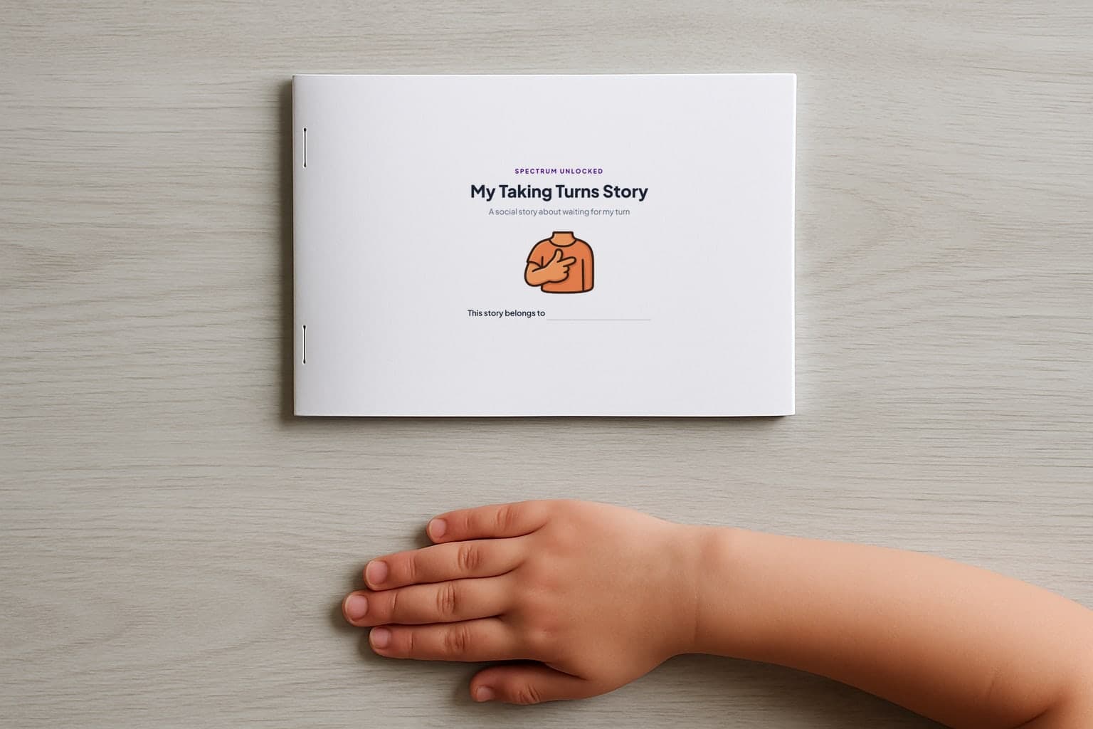 The Taking Turns social story printed and stapled into a small booklet, closed on a table with a child's hand beside it