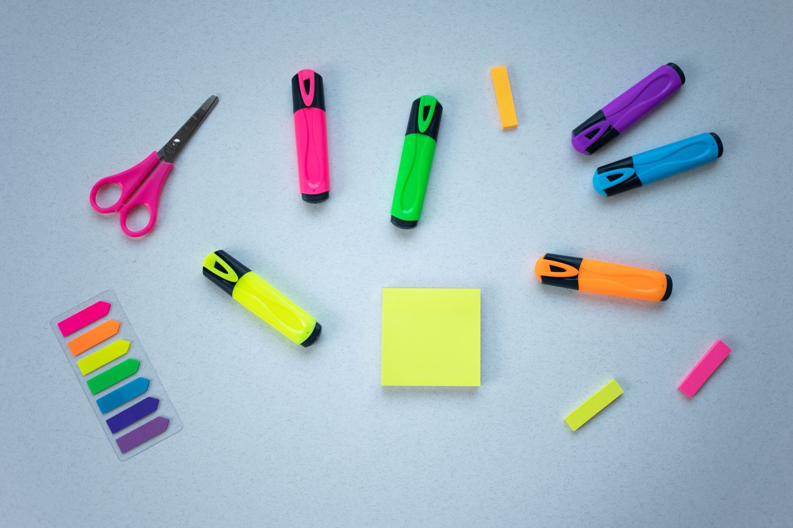 A colorful flat lay of highlighters, sticky notes, and scissors arranged on a light background, styled for a teacher classroom supply wishlist