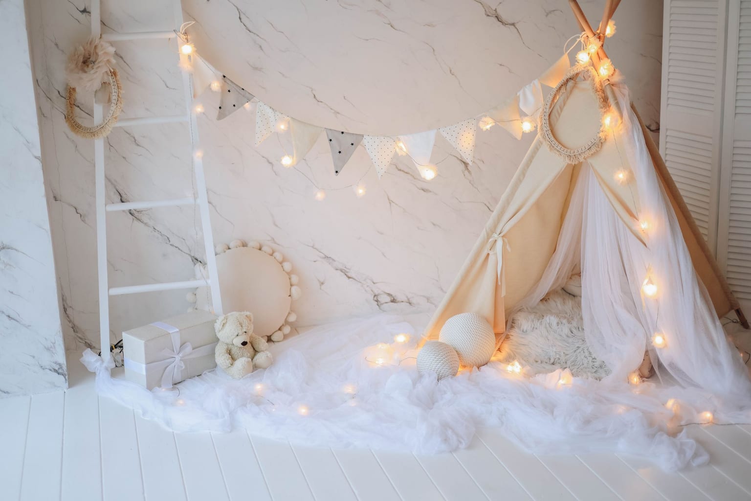A play tent strung with warm string lights beside a teddy bear, all soft warm light