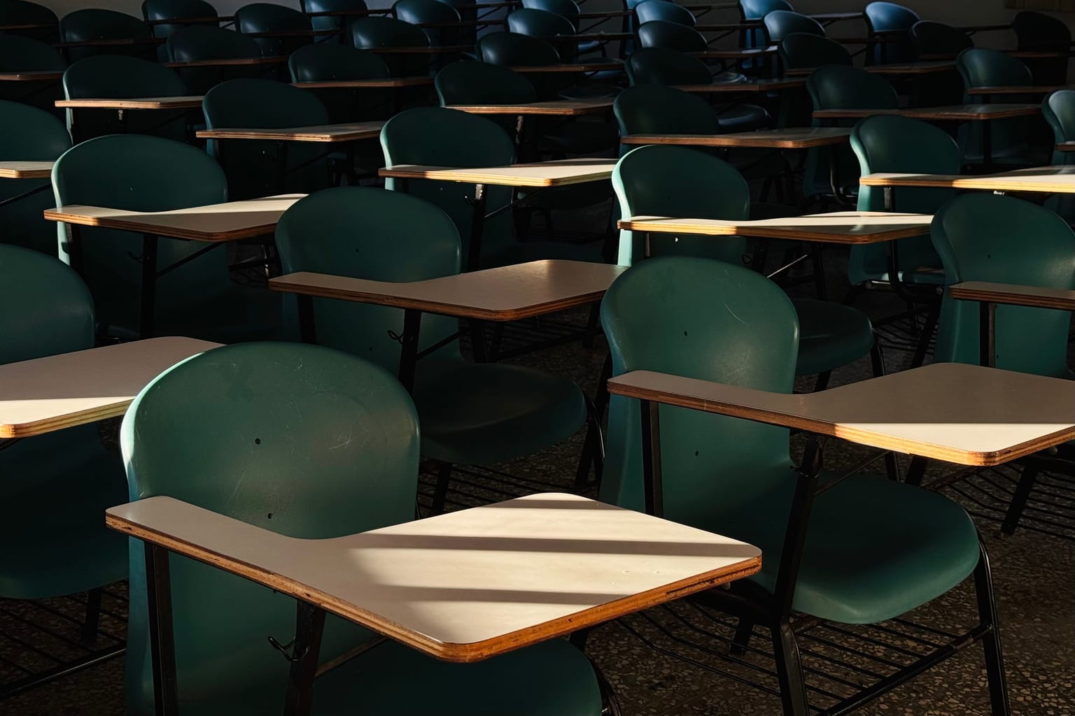 An empty classroom with low sun through blinds falling across the desks