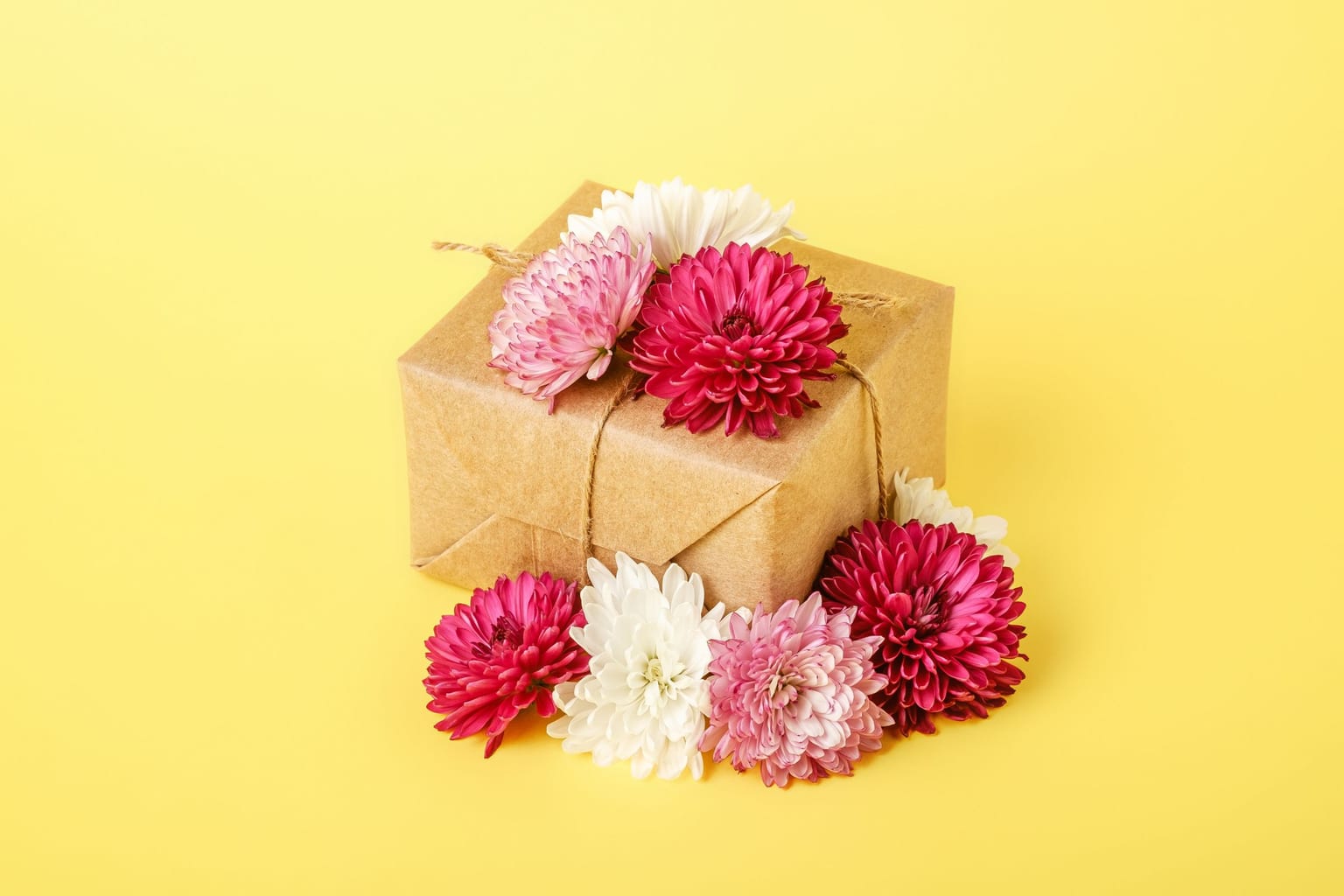 A gift wrapped in kraft paper and twine with pink and white chrysanthemums tucked around it
